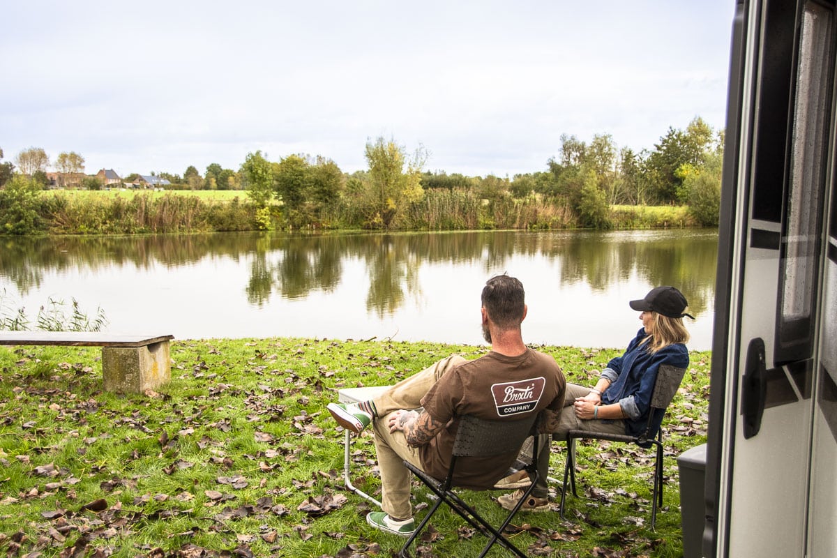 Een paar geniet van een moment van ontspanning voor hun camper, omgeven door de natuurlijke schoonheid van een rustige camping.