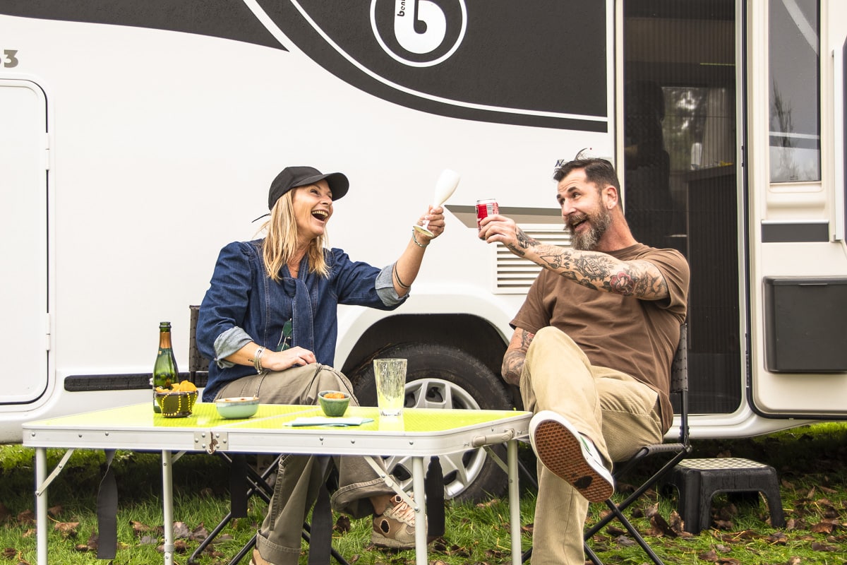 Een echtpaar deelt een vrolijk moment terwijl ze buiten hun camper toasten op hun kampeeravontuur.