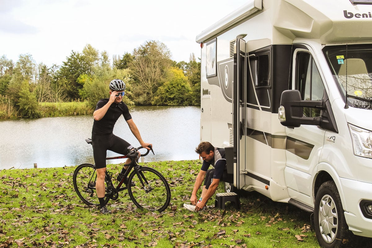 Camper huren met fiets. Twee wielrenners bereiden zich voor op een fietstocht bij hun Reislust camper, omgeven door natuur.