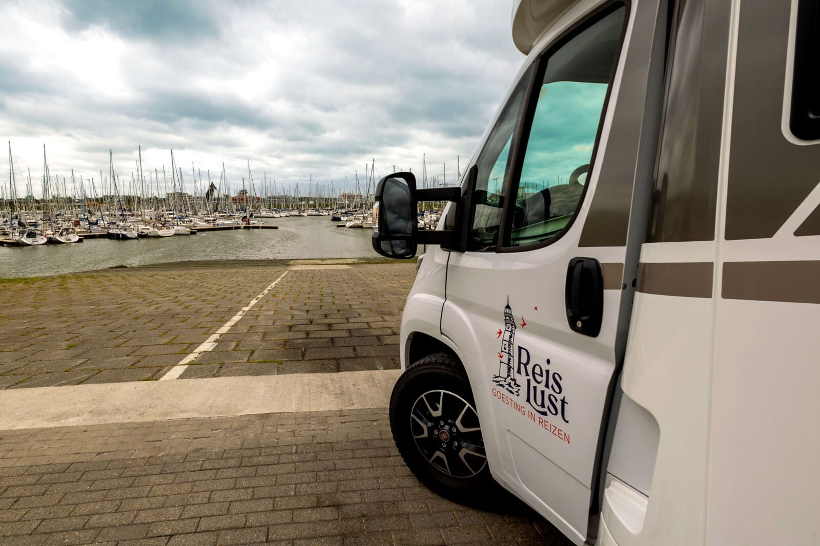 Zijaanzicht van een Reislust camper geparkeerd aan een jachthaven met meerdere boten op de achtergrond.